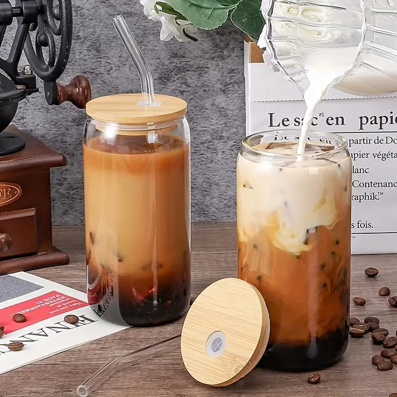 Dois copos de vidro com tampa de bambu, cheios de café gelado cremoso em uma bancada.