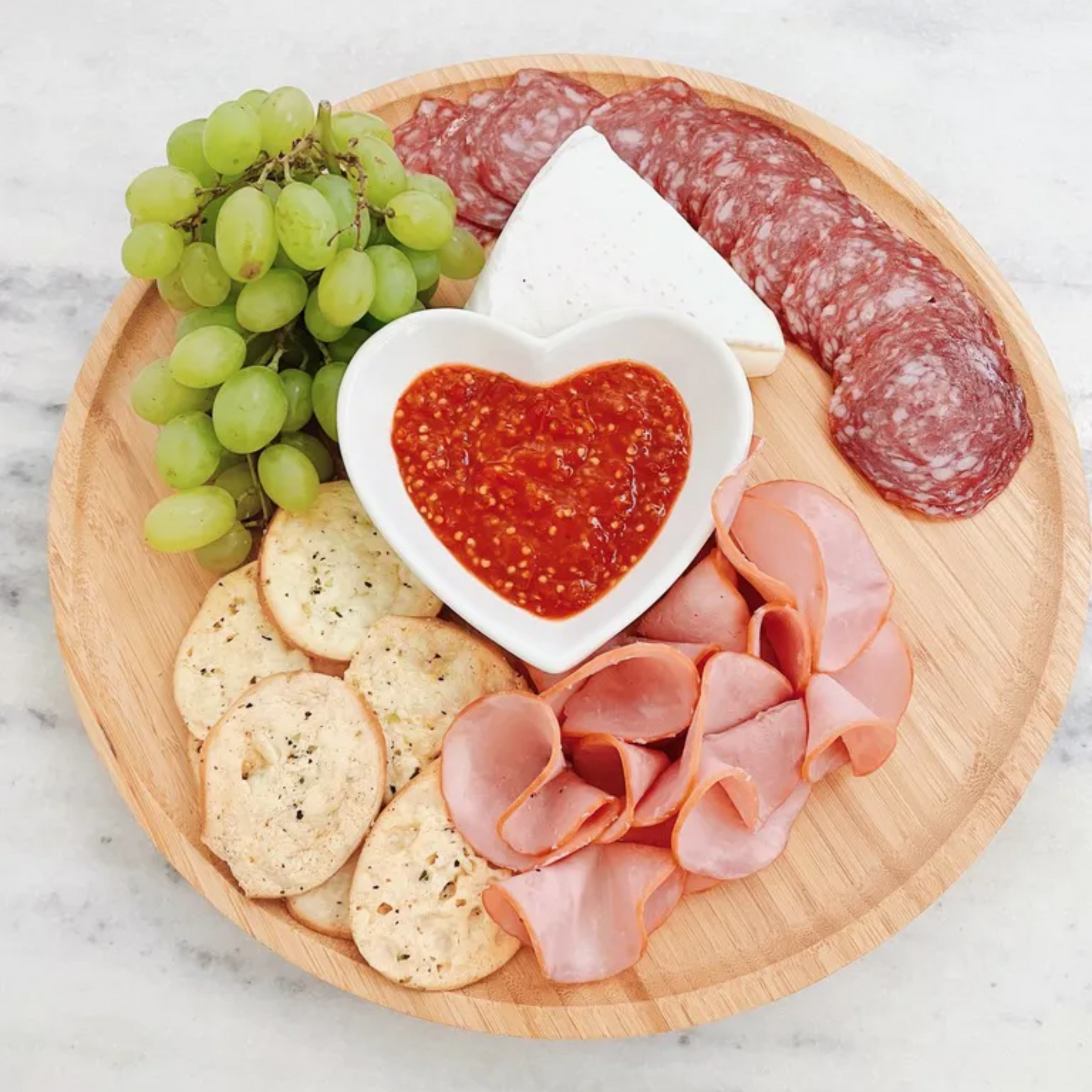 Bandeja giratória de bambu servindo como tábua de frios com salame, queijo, uvas e bolachas.