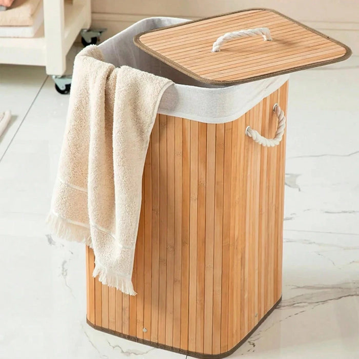 Cesto de lavanderia de bambu com tampa e uma toalha bege pendurada na lateral, em um ambiente de banheiro.