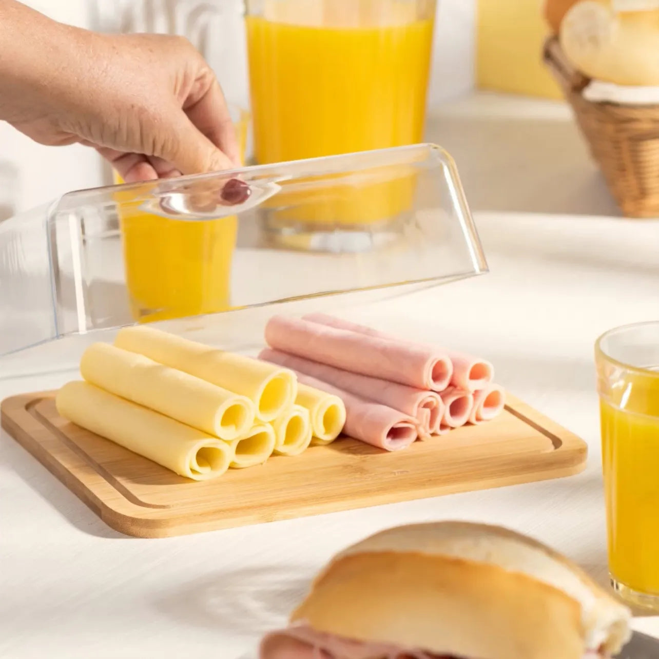 Mesa de café da manhã com porta-frios de bambu com rolinhos de presunto e queijo sendo servidos.