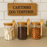Potes de vidro com tampa de bambu e colher, armazenando açúcar, café e castanhas em cantinho de temperos.
