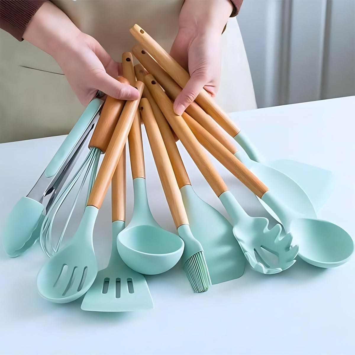 Mãos segurando um kit de utensílios de cozinha com cabo de bambu e pontas de silicone na cor verde menta.