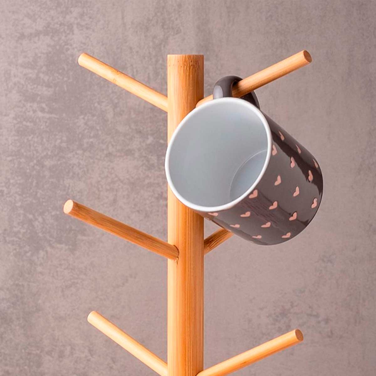 Close-up do topo de um suporte de bambu, com uma caneca escura de bolinhas pendurada em um dos ganchos.