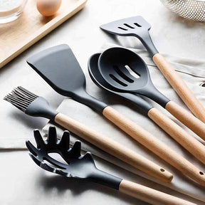 Close-up de diversos utensílios de silicone e bambu, incluindo espátula e pegador de massa, sobre uma superfície de madeira.