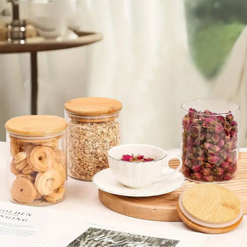 Potes de vidro com tampa de bambu armazenando biscoitos, chá seco e cereais para café da manhã

