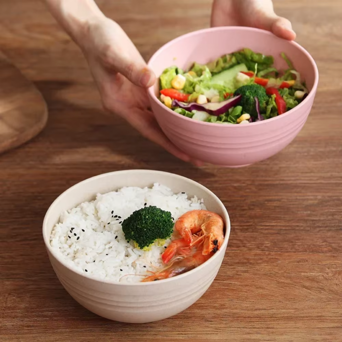 Tigela de fibra de bambu na cor bege com arroz e camarão, e mãos segurando uma tigela rosa com salada.