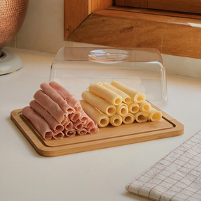 Porta-frios de bambu com tampa, armazenando rolinhos de salame e queijo em uma prateleira.