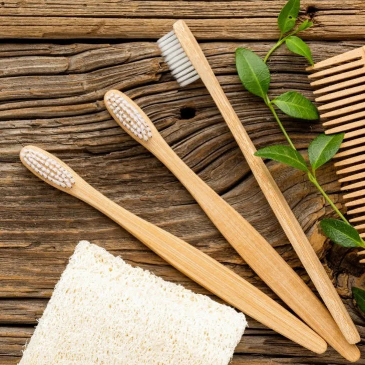 Escovas de dente ecológicas de bambu sobre superfície de madeira rústica com pente e bucha vegetal.
