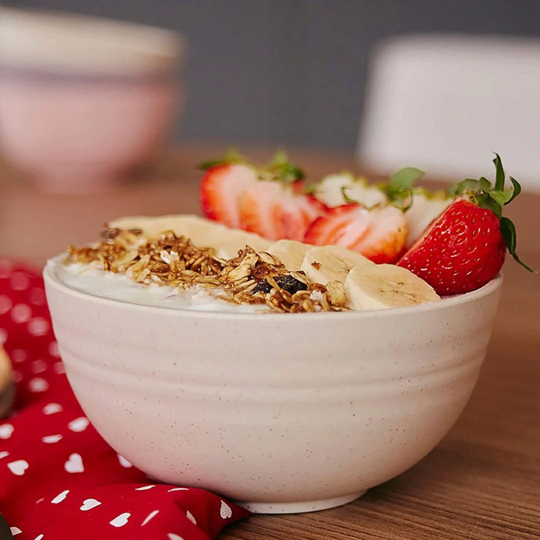 Tigela de fibra de bambu na cor bege servindo cereal com fatias de banana e morango.