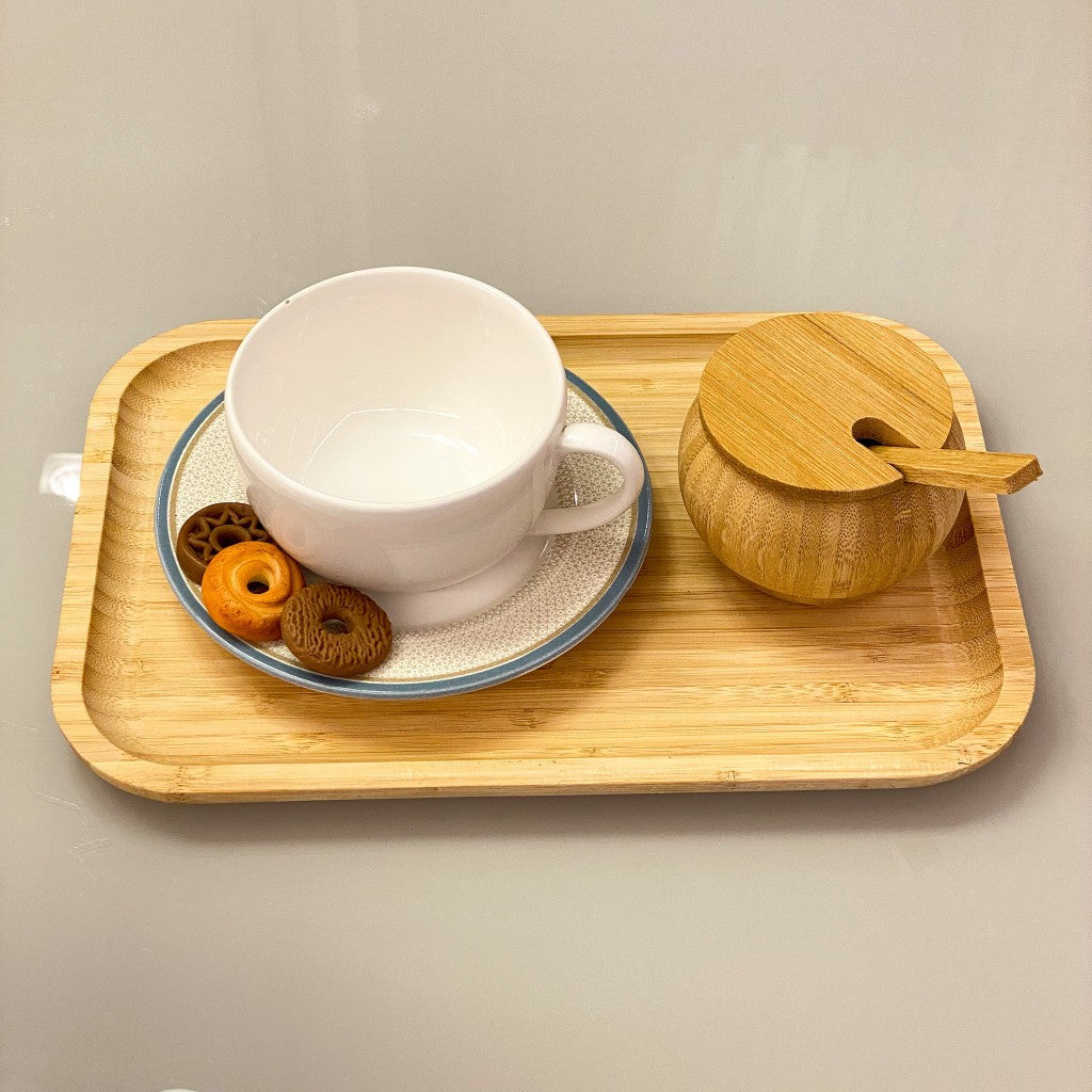 Bandeja de bambu com xícara branca, pires, colher de bambu e biscoitos

