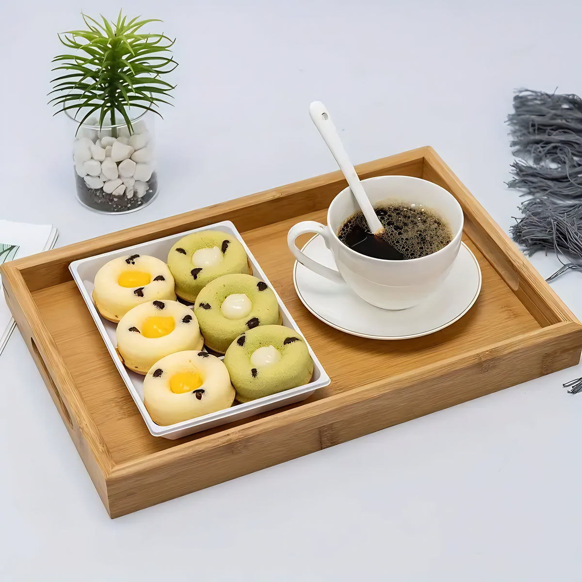 Bandeja retangular de bambu servindo uma xícara de café e um prato com pães de queijo em uma mesa branca.
