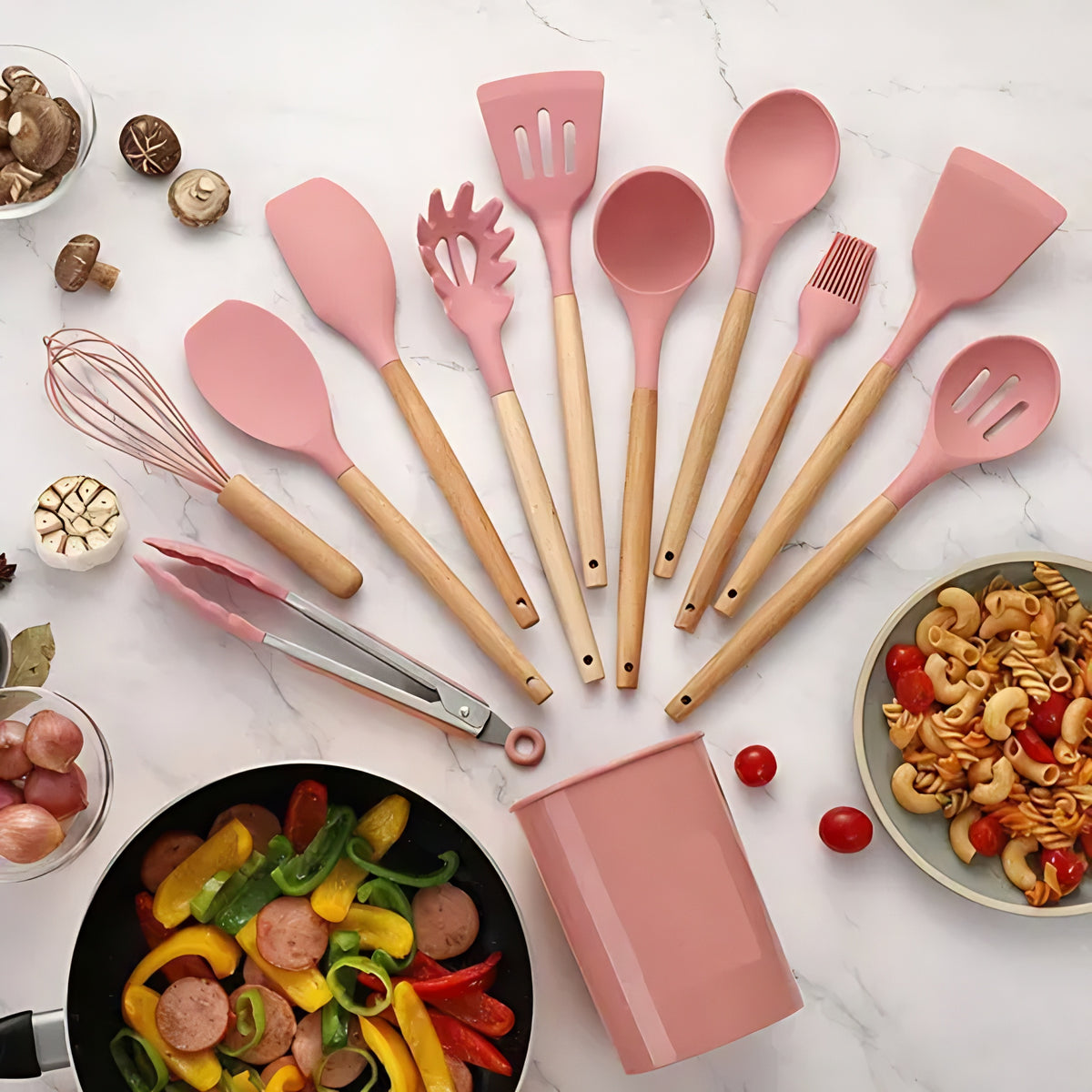 Kit completo de utensílios de cozinha com pontas de silicone rosa e cabos de bambu, ao lado de um pote com macarrão.